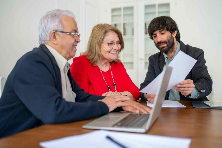 Two senior clients and a younger advisor reviewing accessible documents on a laptop
