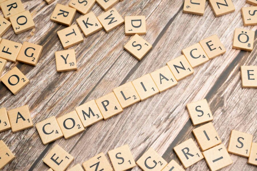 Scrabble tiles arranged to spell the word COMPLIANCE on a wooden surface
