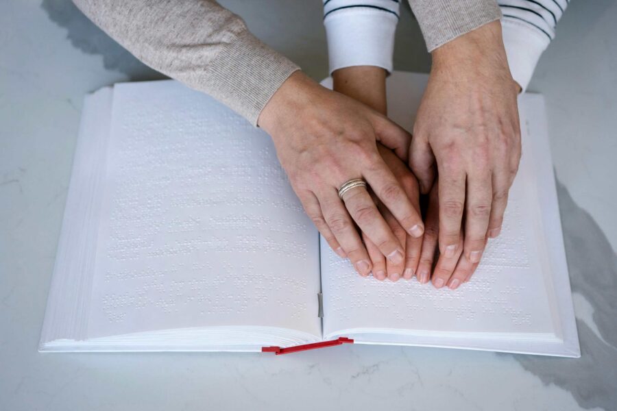 Two people with hands on an open braille book learning to read tactile text