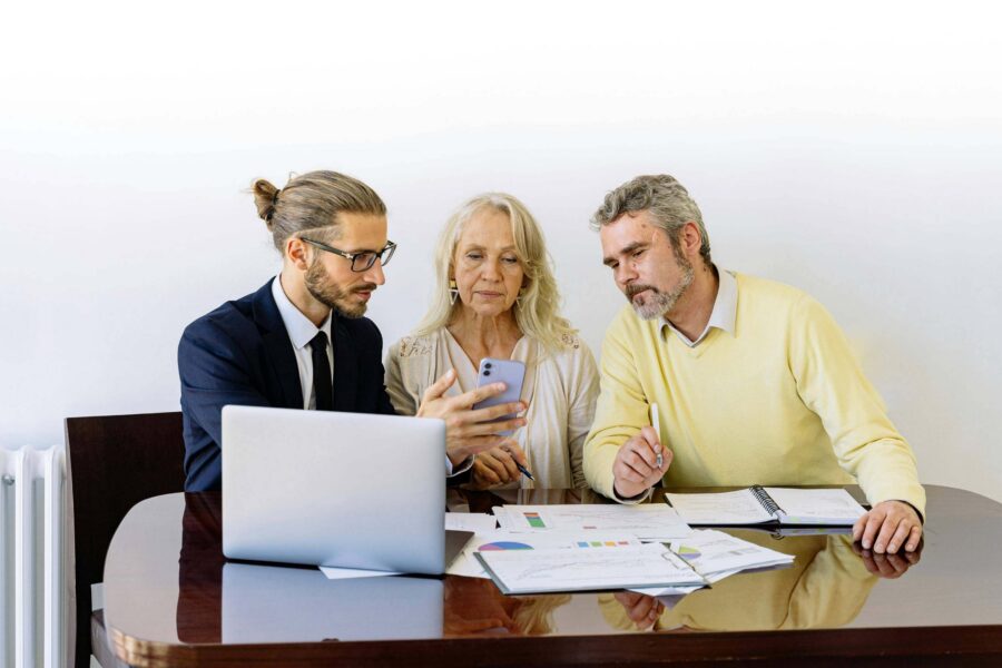 Financial advisor showing digital document on phone to older couple with printed charts on desk