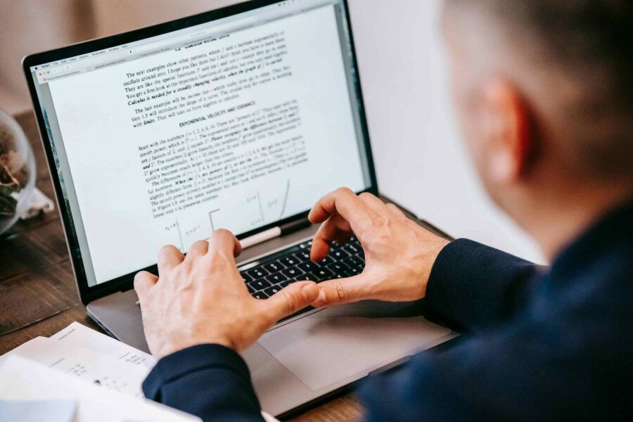 Man reading text-heavy document on laptop screen showing educational content for compliance research