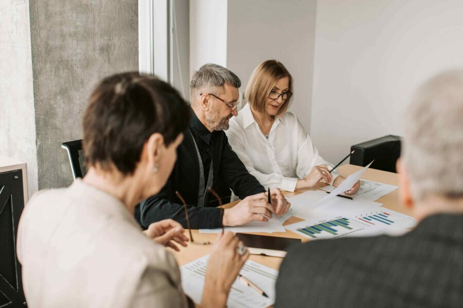 Four business professionals reviewing printed charts and documents together at conference table